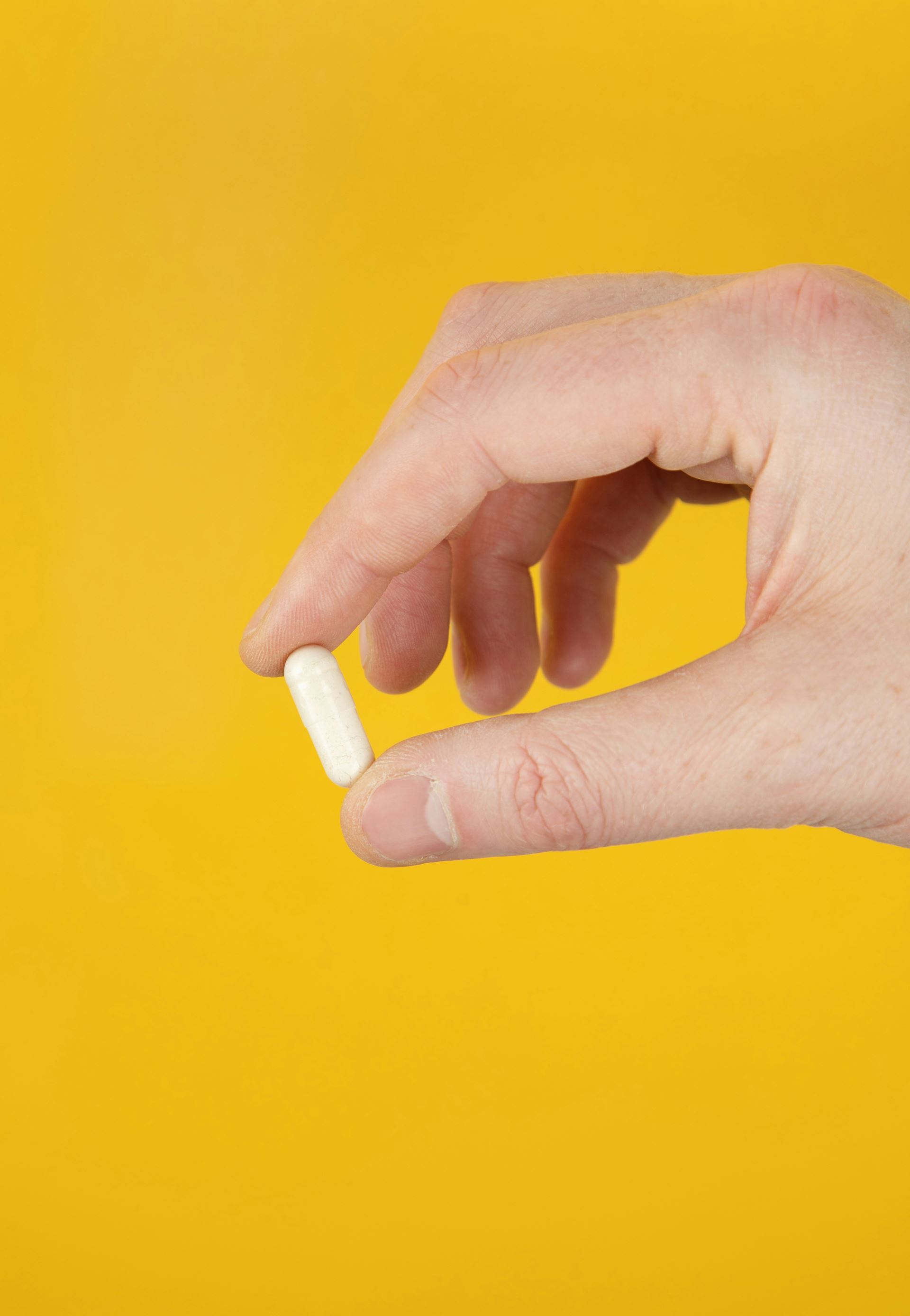 a hand holding a supplement capsules between their finger and thumb