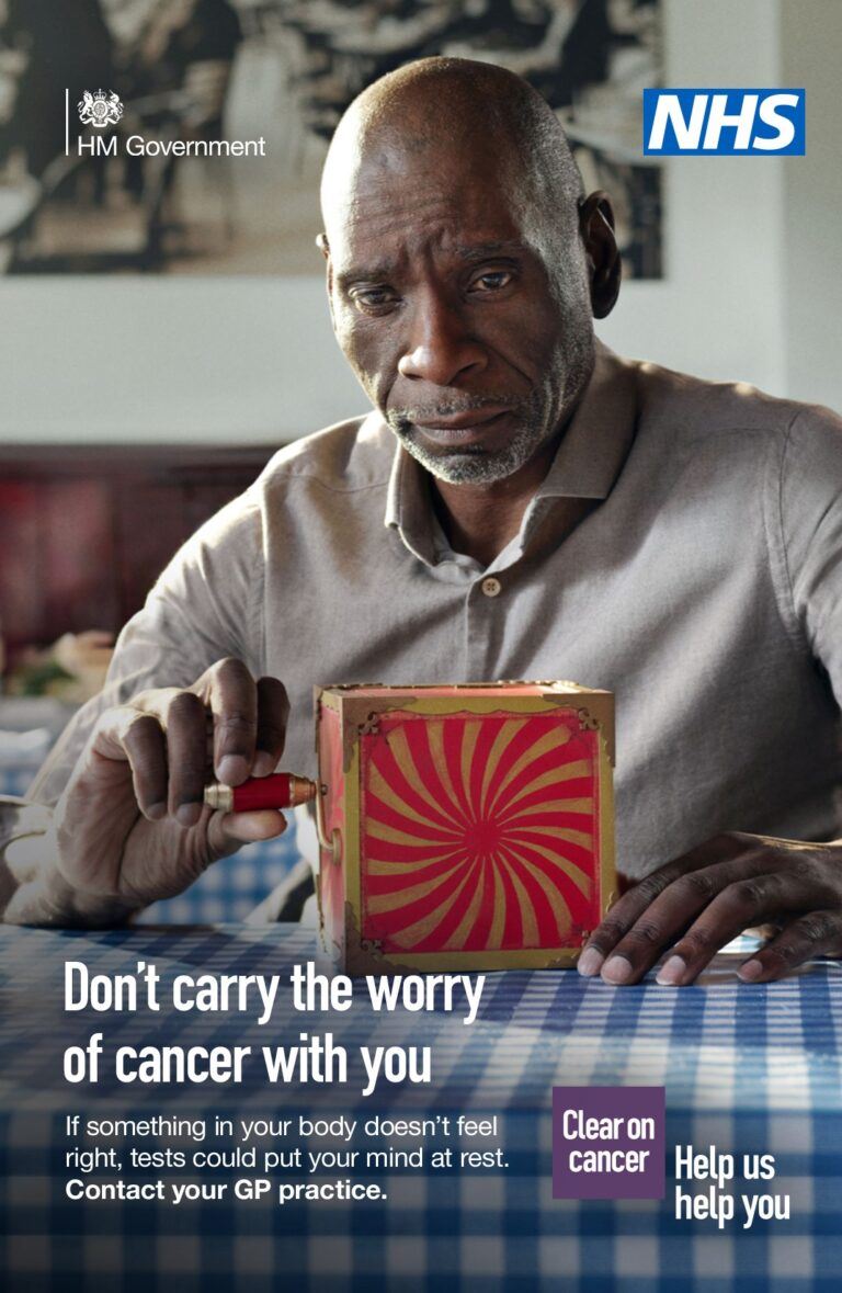 A middle-aged person sitting a cafe with a red jack-in-the-box toy on the table across from them. The person is looking at the red-jack-in-the-box with a concerned expression on their face. The text reads: Don’t carry the worry of cancer with you. The NHS logo is in the top right hand corner.