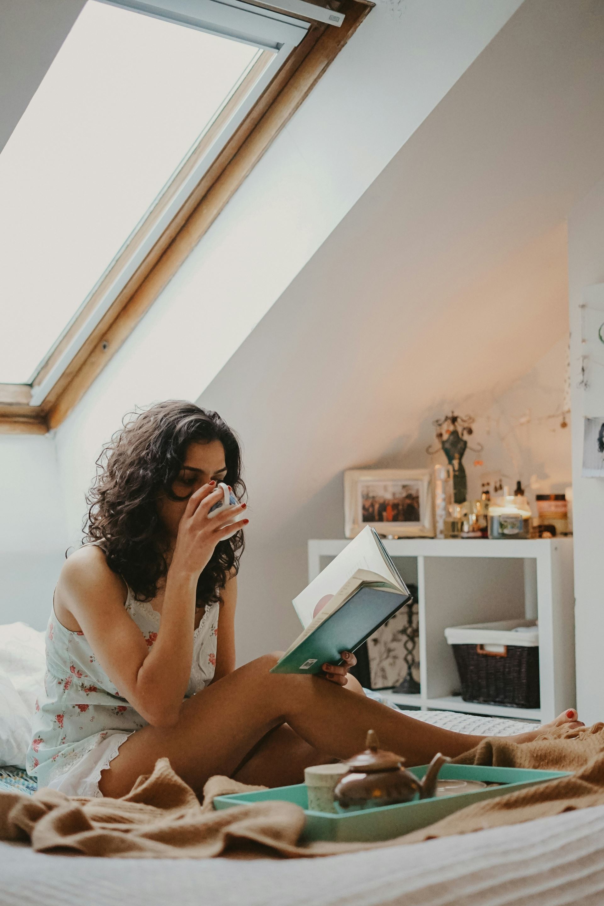 a woman sat reading a book and drinking a cup of coffee